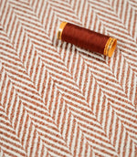 Chestnut-coloured thread spool resting on Bampton Chestnut herringbone fabric, highlighting the coordinating orange-brown tones and off-white chevron weave.