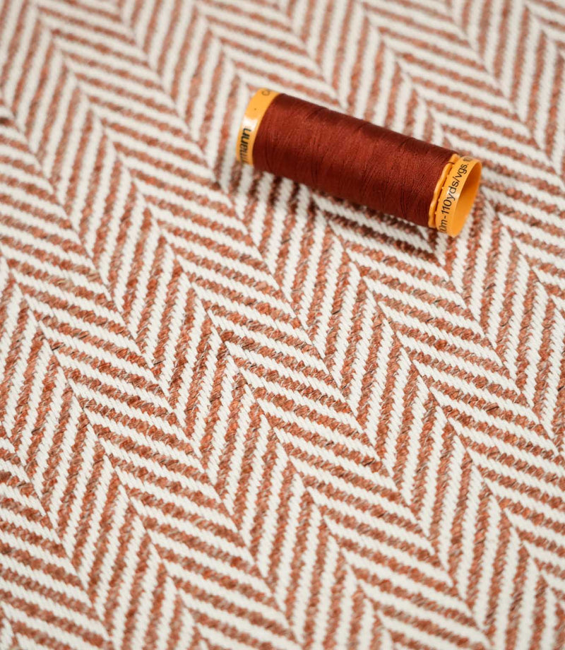 Chestnut-coloured thread spool resting on Bampton Chestnut herringbone fabric, highlighting the coordinating orange-brown tones and off-white chevron weave.