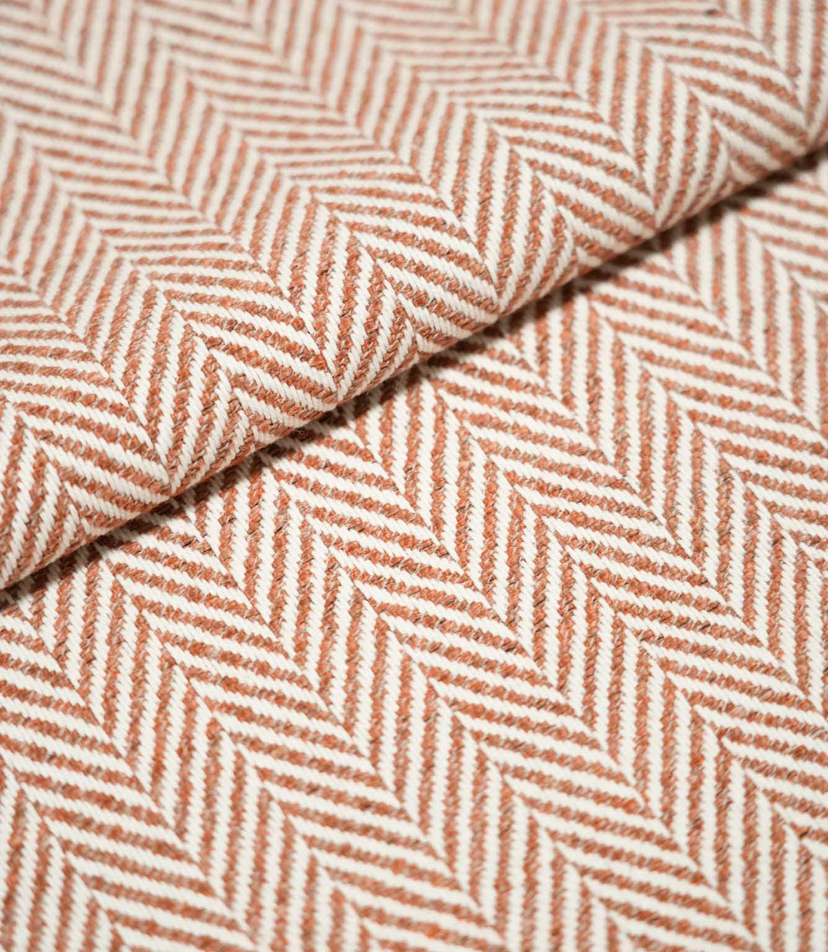 Close-up of folded Bampton Chestnut herringbone fabric, showing the substantial woven texture, thickness and repeating chestnut orange and off-white chevron pattern.