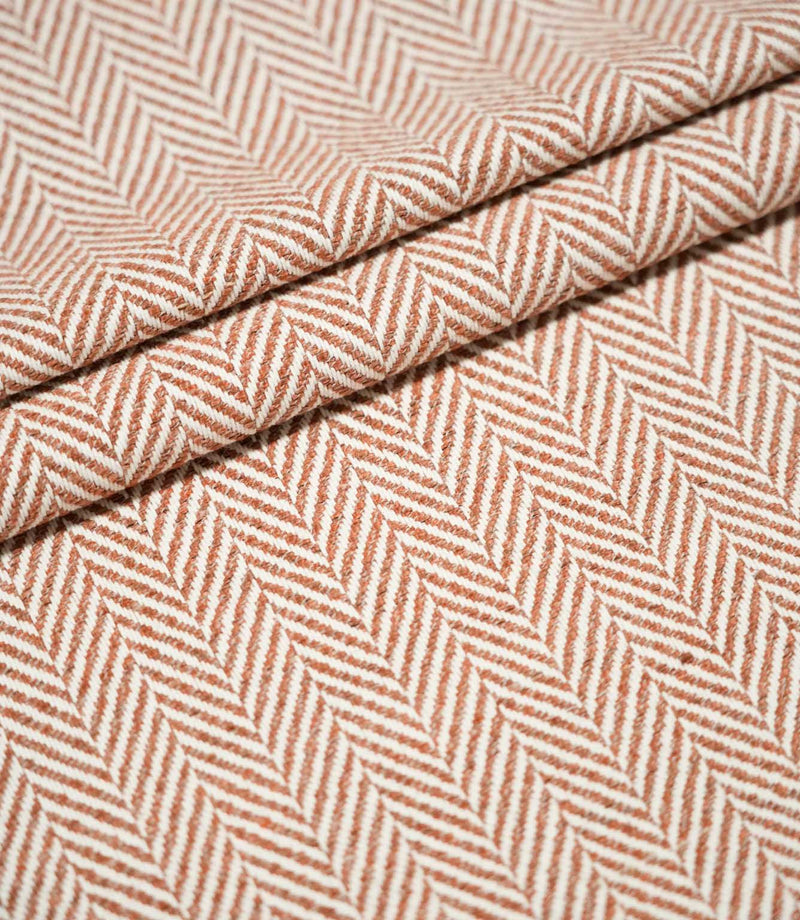 Layered folds of Bampton Chestnut herringbone fabric, showing the fabric's structure, thickness and repeating orange-brown and off-white chevron pattern.