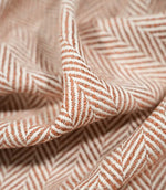 Macro close-up of draped Bampton Chestnut herringbone fabric, highlighting the individual woven fibres, textured surface and detailed orange-brown and off-white chevron design.