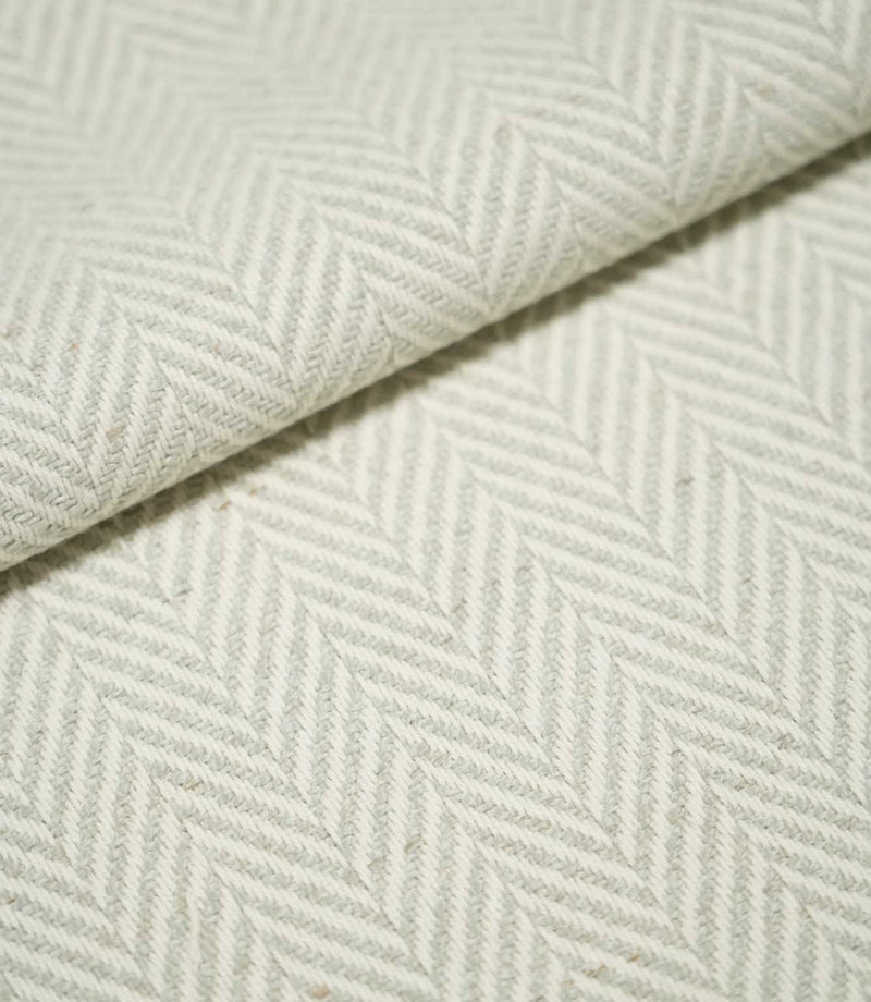 Close-up of folded Bampton Elephant Grey herringbone fabric, showing the soft grey and off-white chevron pattern, woven texture and substantial finish.