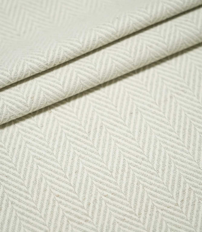 Layered folds of Bampton Elephant Grey herringbone fabric, highlighting the repeating neutral chevron pattern, textured weave and fabric thickness.