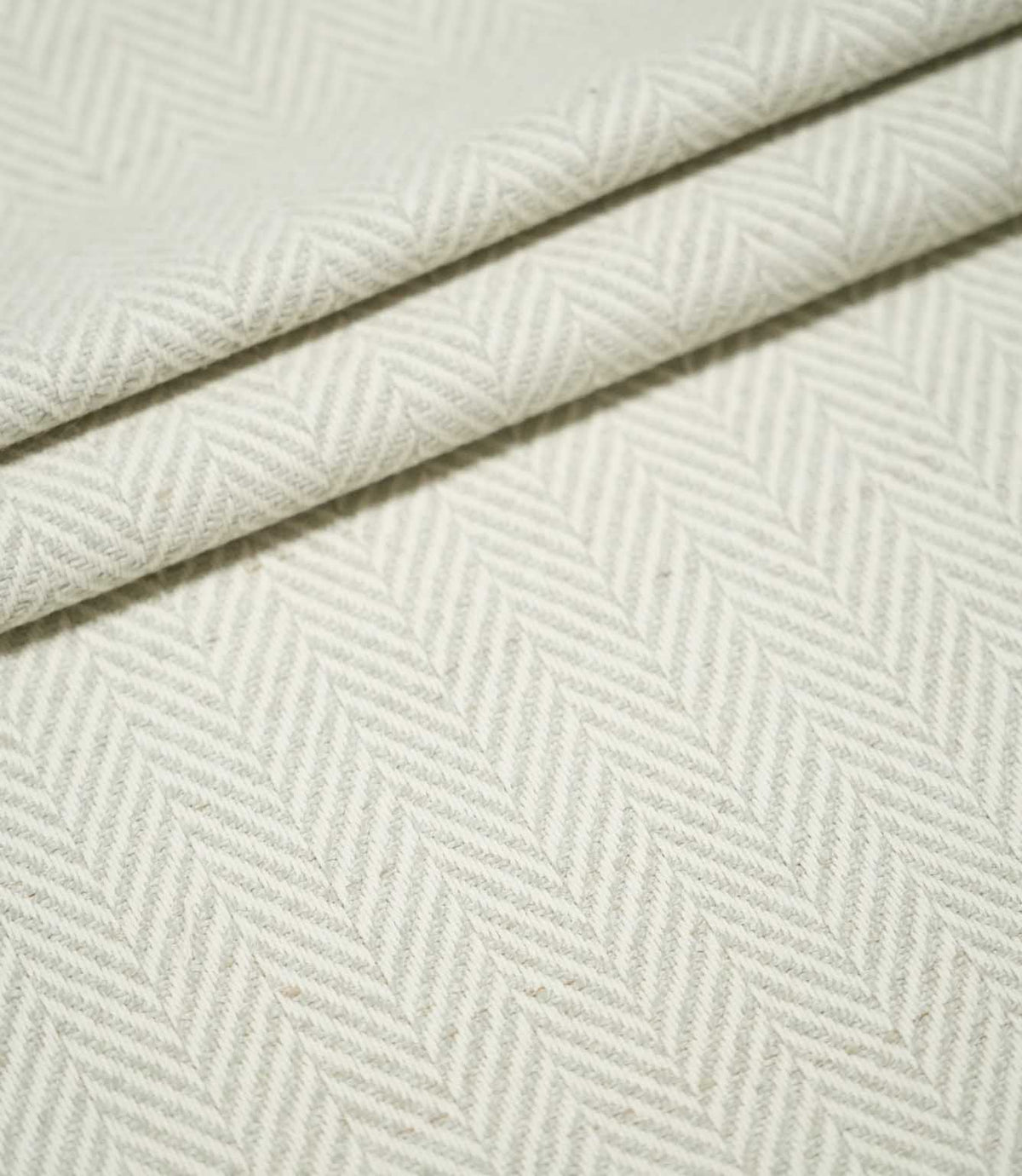 Layered folds of Bampton Elephant Grey herringbone fabric, highlighting the repeating neutral chevron pattern, textured weave and fabric thickness.