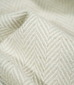 Macro close-up of Bampton Elephant Grey herringbone fabric draped into a soft fold, revealing the detailed pale grey and off-white weave, individual fibres and tactile texture.