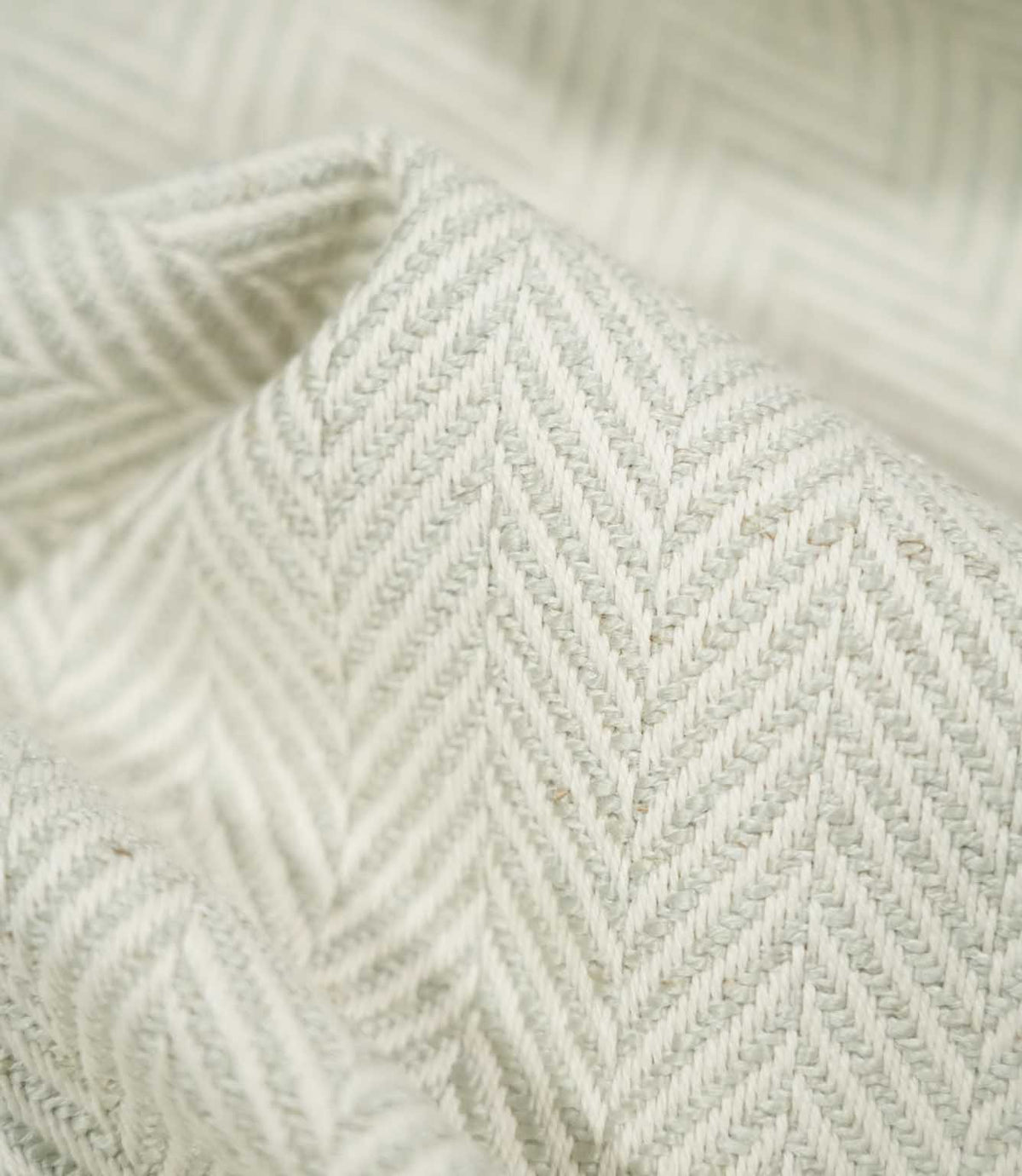 Macro close-up of Bampton Elephant Grey herringbone fabric draped into a soft fold, revealing the detailed pale grey and off-white weave, individual fibres and tactile texture.