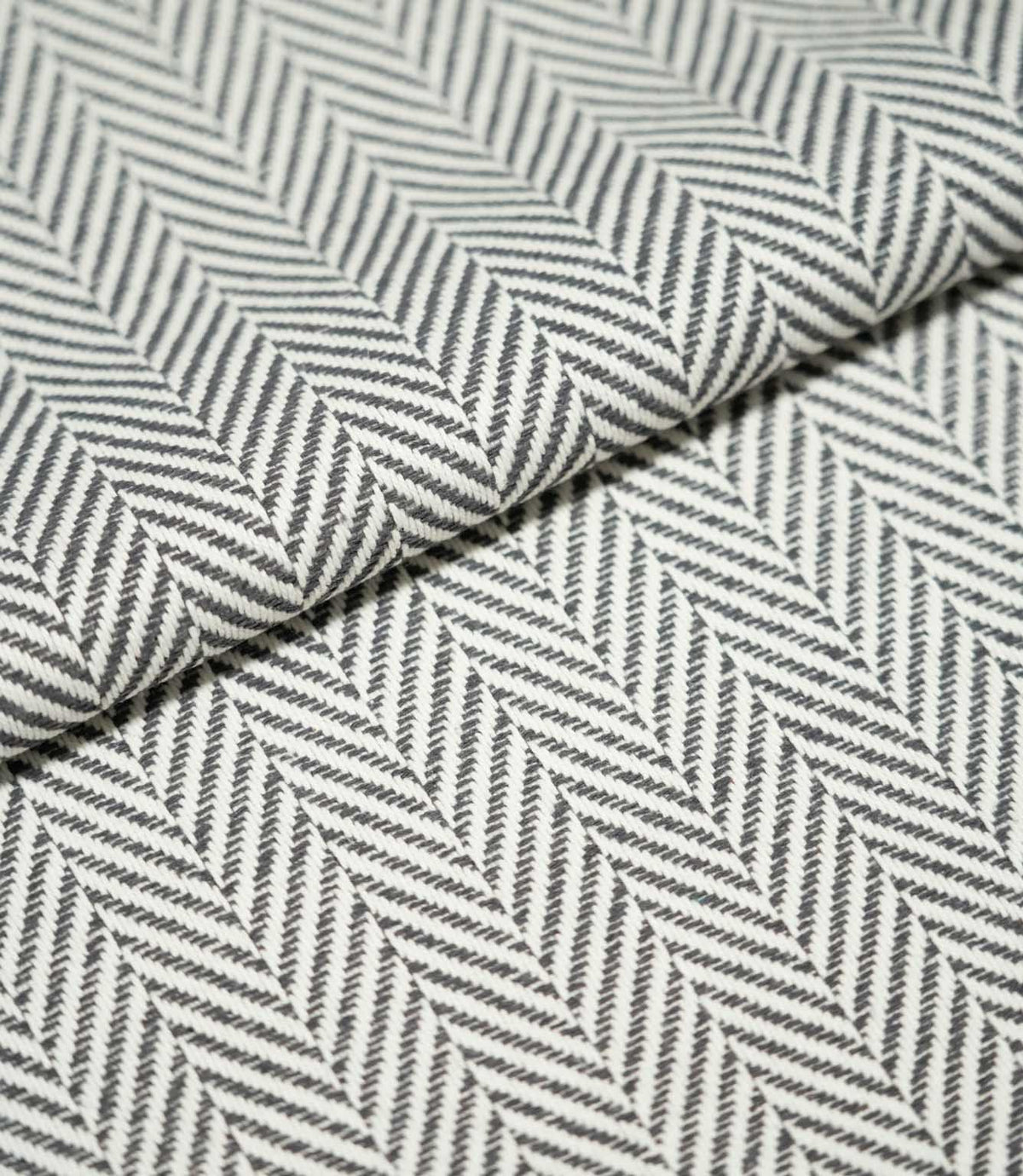 Close-up of folded Bampton Grey herringbone fabric, highlighting the structured woven texture, grey and off-white chevron pattern and fabric thickness.