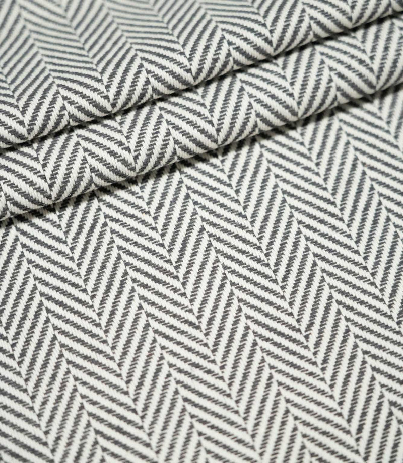 Bampton Grey herringbone upholstery fabric arranged in neat folds, showing the repeating grey and off-white woven pattern and substantial textured finish.