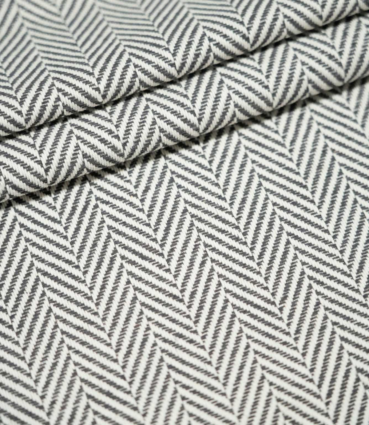 Bampton Grey herringbone upholstery fabric arranged in neat folds, showing the repeating grey and off-white woven pattern and substantial textured finish.