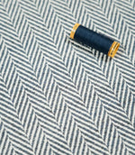 Navy thread spool resting on Bampton Ink herringbone fabric, highlighting the coordinating deep blue tones, off-white chevron pattern and tactile woven texture.