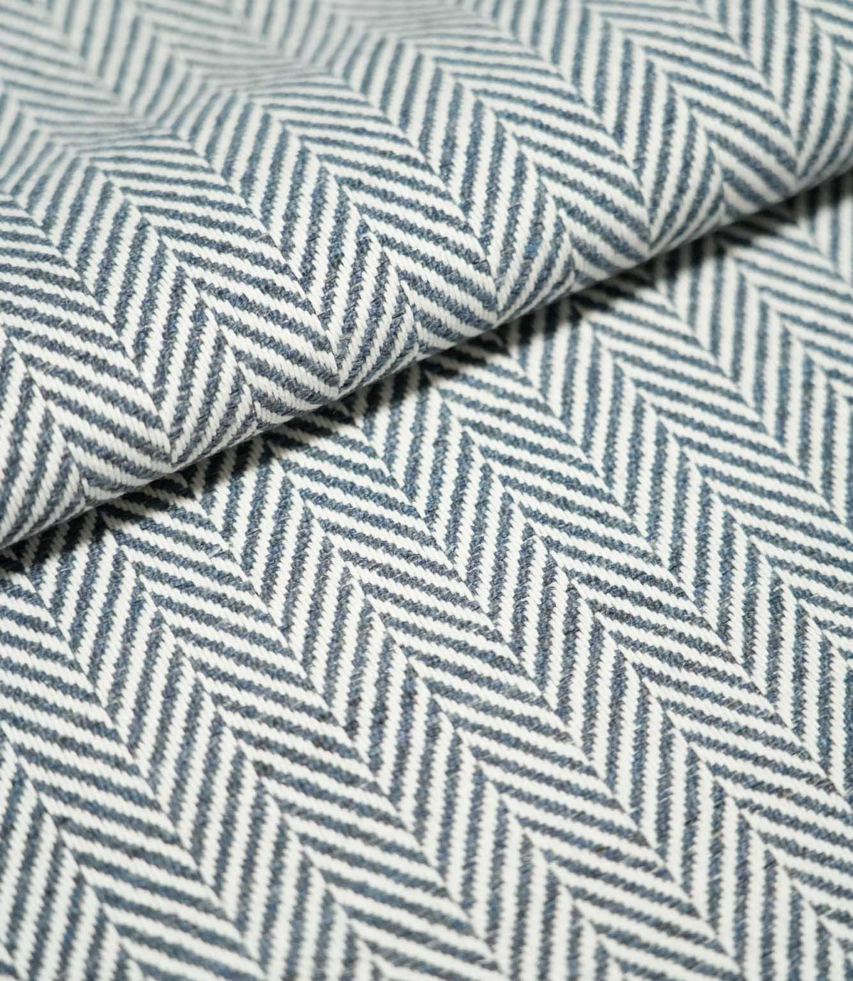 Close-up of folded Bampton Ink herringbone fabric, showing its substantial woven texture and repeating navy blue and off-white chevron design.