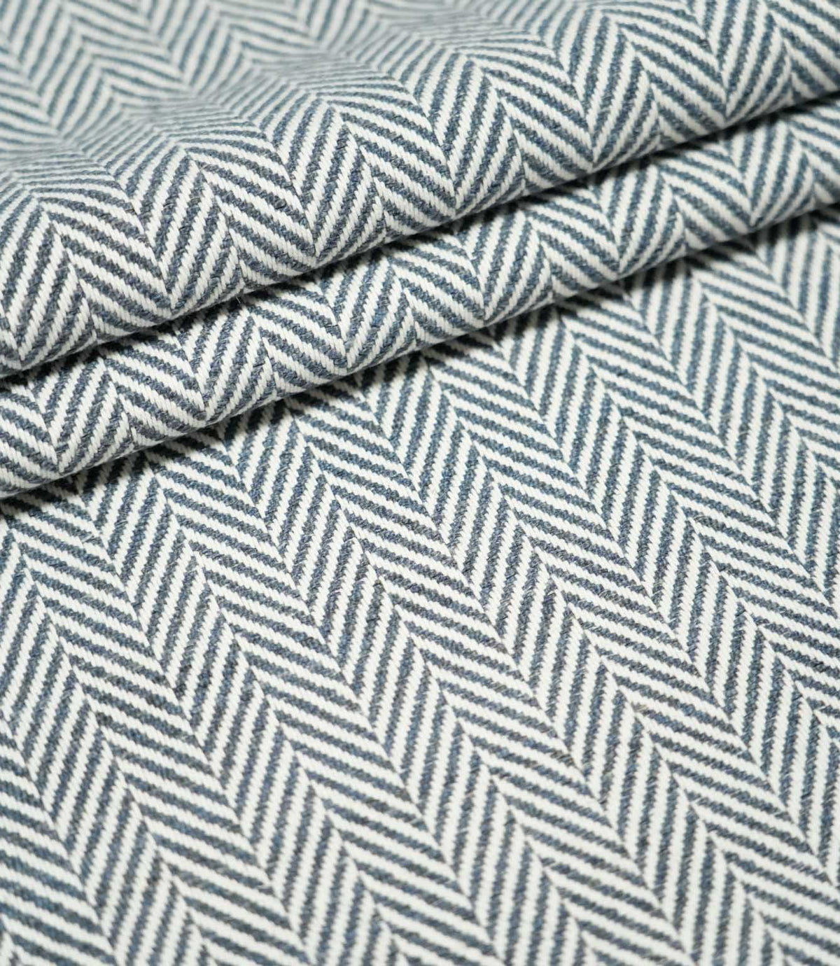 Layered folds of Bampton Ink herringbone fabric, highlighting the structured weave, thickness and contrasting navy blue and off-white herringbone pattern.