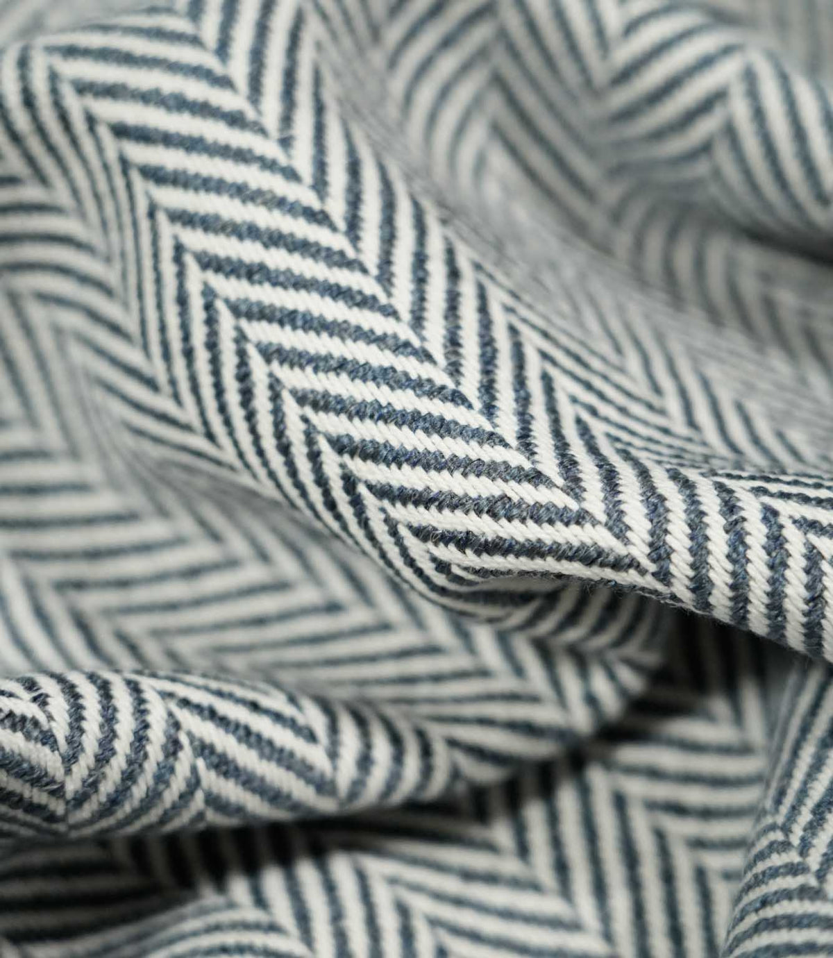 Macro close-up of draped Bampton Ink herringbone fabric, highlighting the individual woven fibres, fabric thickness and detailed navy blue and off-white herringbone pattern.