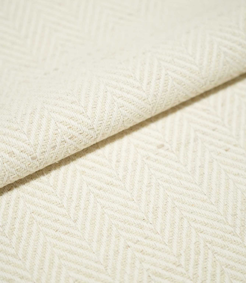 Close-up of folded Bampton Jasmine herringbone fabric, showing the thickness of the material and its subtle cream chevron weave with natural flecked detail.