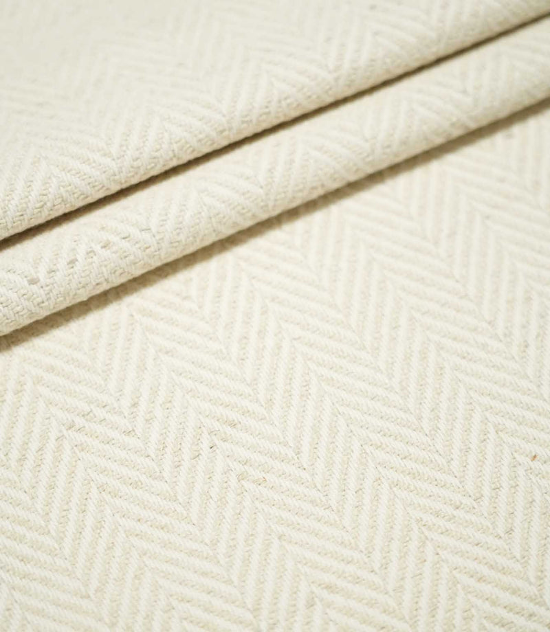 Bampton Jasmine herringbone fabric arranged in layered folds, displaying the tonal cream chevron pattern and substantial textured woven finish.