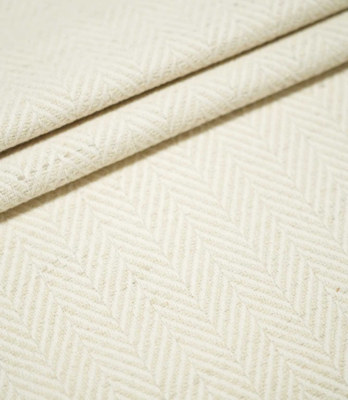 Bampton Jasmine herringbone fabric arranged in layered folds, displaying the tonal cream chevron pattern and substantial textured woven finish.