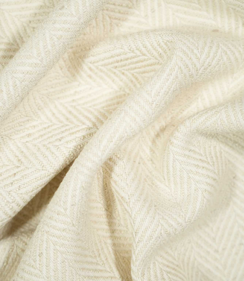 Bampton Jasmine herringbone fabric loosely draped and gathered, demonstrating the natural movement of the material and its subtle cream woven chevron pattern.
