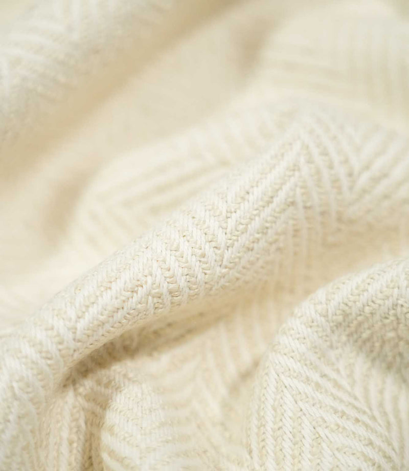 Macro close-up of draped Bampton Jasmine herringbone fabric, highlighting the individual woven fibres, raised texture and understated cream chevron design.