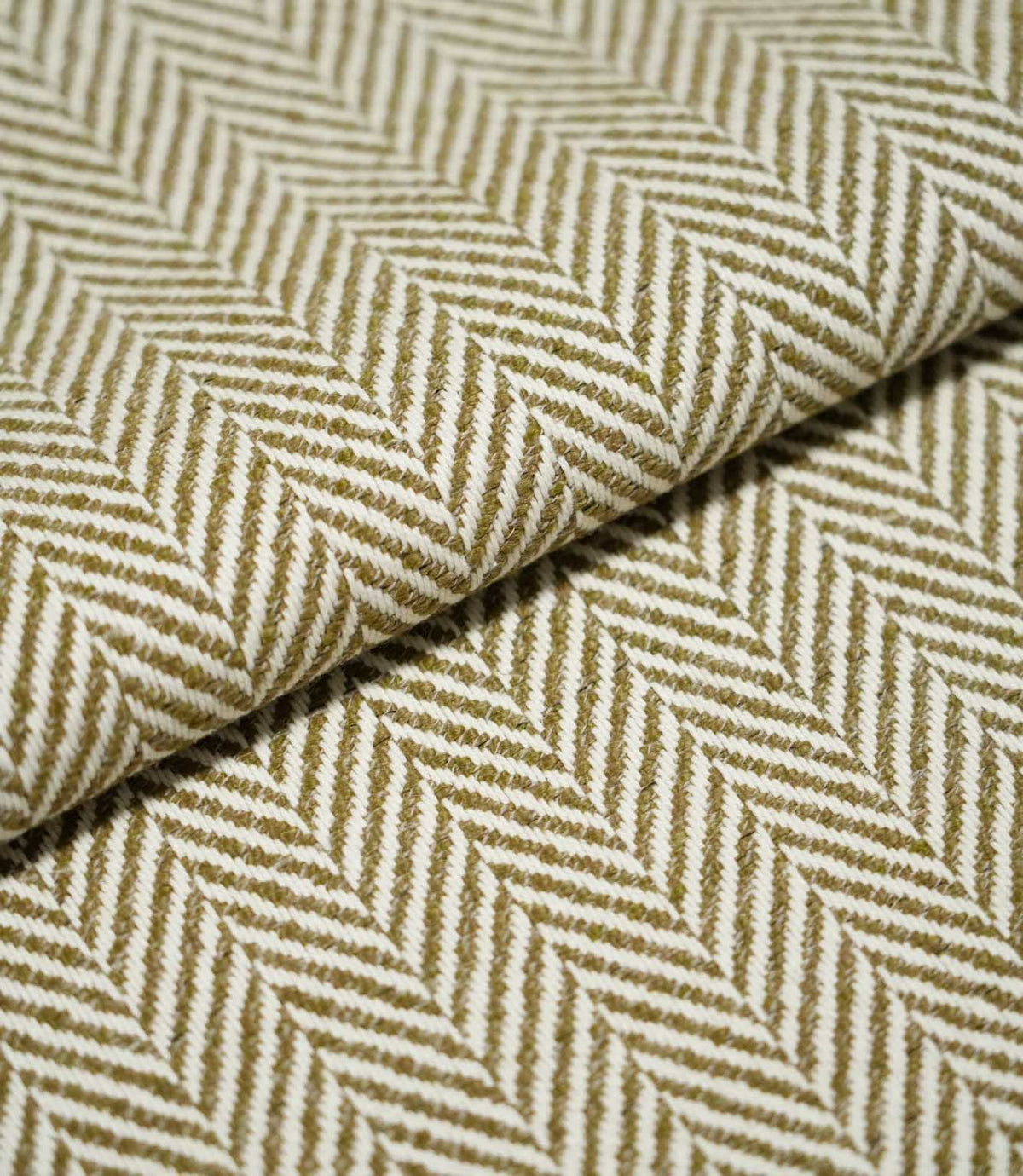 Close-up of folded Bampton Matcha herringbone fabric, showing the substantial woven texture, fabric thickness and repeating olive green and off-white chevron pattern.