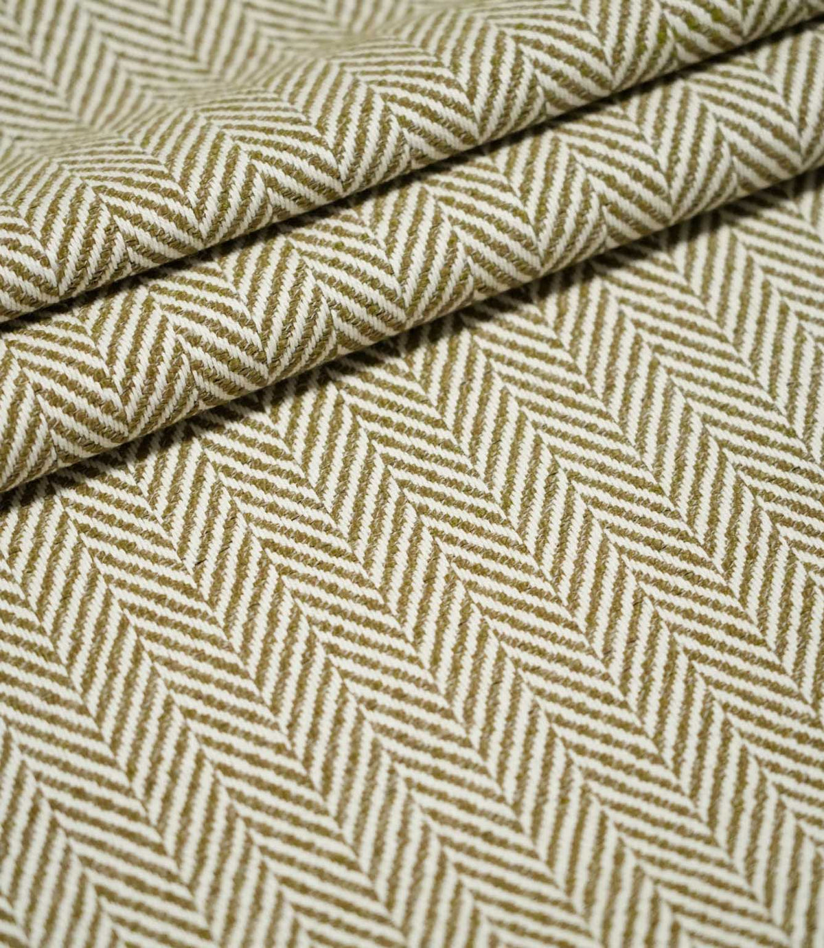 Bampton Matcha herringbone fabric arranged in layered folds, displaying the structured texture and repeating olive green and off-white woven chevron design.