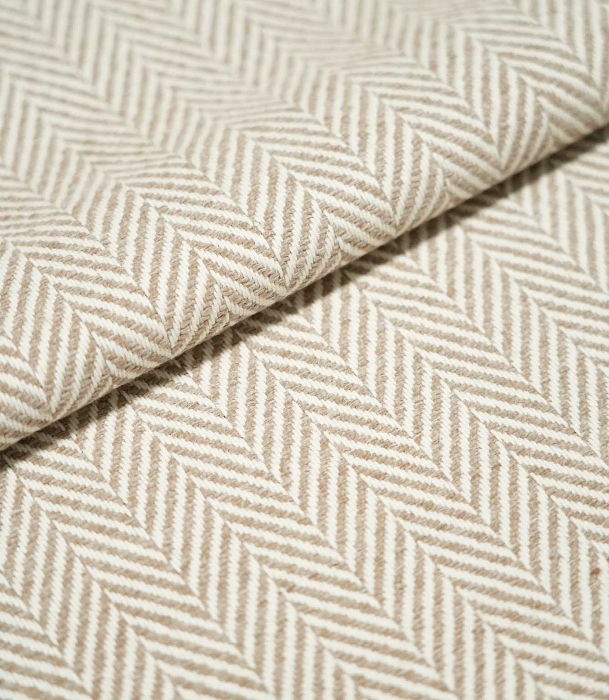 Close-up of folded Bampton Taupe herringbone fabric, showing the warm taupe and off-white chevron pattern, raised woven texture and substantial finish.