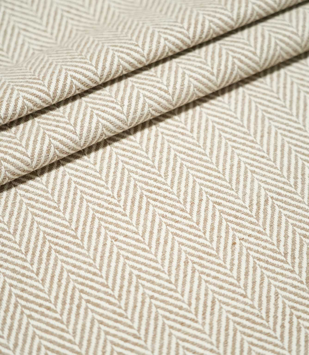 Layered folds of Bampton Taupe herringbone fabric, highlighting the repeating neutral chevron design, textured weave and fabric thickness.