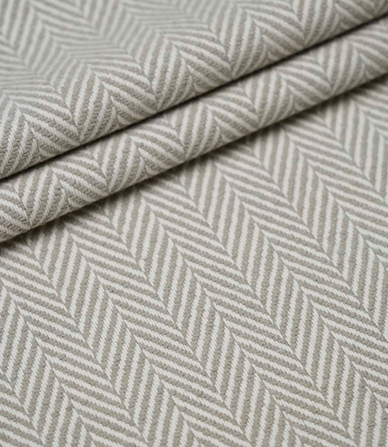 Layered Bampton Argent woven fabric featuring a timeless chevron herringbone design with a textured finish, suitable for premium upholstery and interior projects.