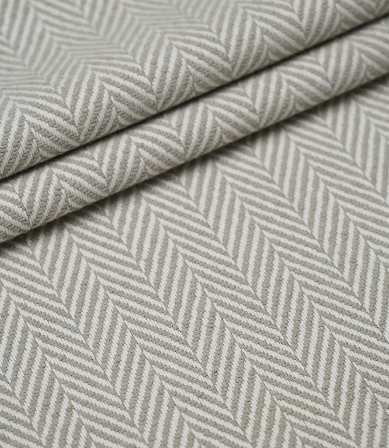 Layered Bampton Argent woven fabric featuring a timeless chevron herringbone design with a textured finish, suitable for premium upholstery and interior projects.