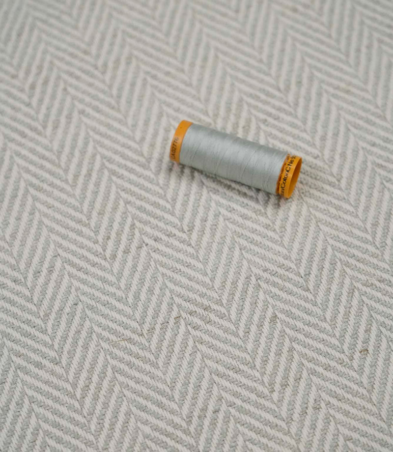 Bampton Elephant Grey woven herringbone upholstery fabric with matching light grey sewing thread, showcasing the textured chevron weave for upholstery and soft furnishing projects.