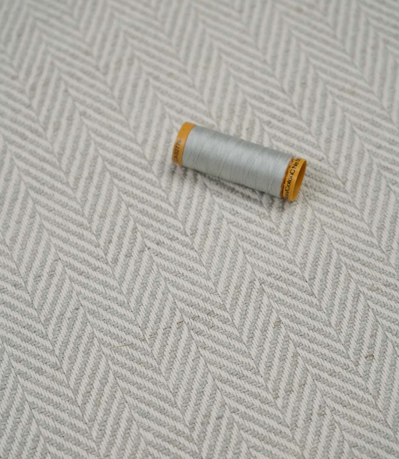 Bampton Elephant Grey woven herringbone upholstery fabric with matching light grey sewing thread, showcasing the textured chevron weave for upholstery and soft furnishing projects.