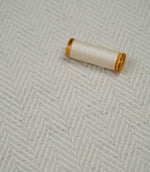 Bampton Jasmine herringbone upholstery fabric with a matching thread spool highlighting the fabric texture and weave.