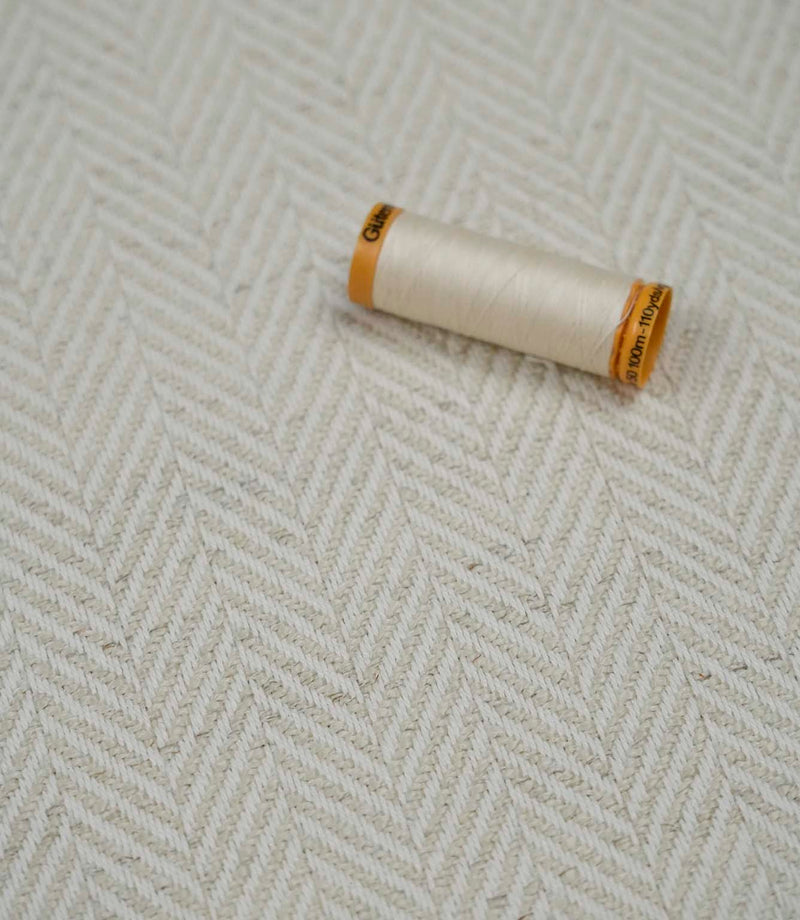 Bampton Jasmine herringbone upholstery fabric with a matching thread spool highlighting the fabric texture and weave.
