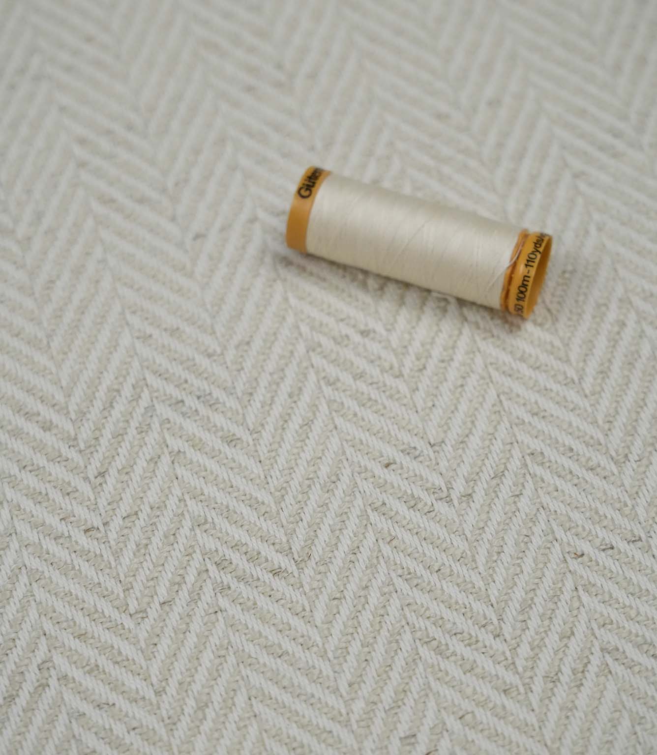 Bampton Jasmine herringbone upholstery fabric with a matching thread spool highlighting the fabric texture and weave.