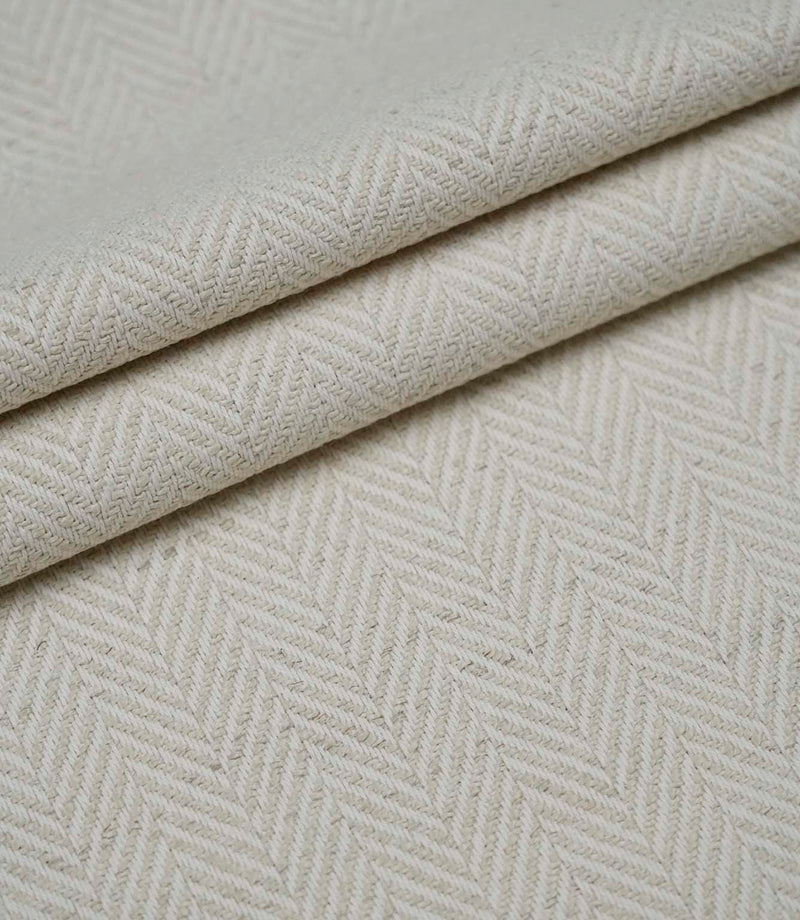 Layered folds of Bampton Jasmine upholstery fabric displaying the woven herringbone pattern and natural finish.
