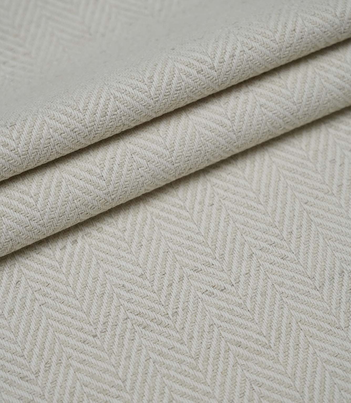 Layered folds of Bampton Jasmine upholstery fabric displaying the woven herringbone pattern and natural finish.