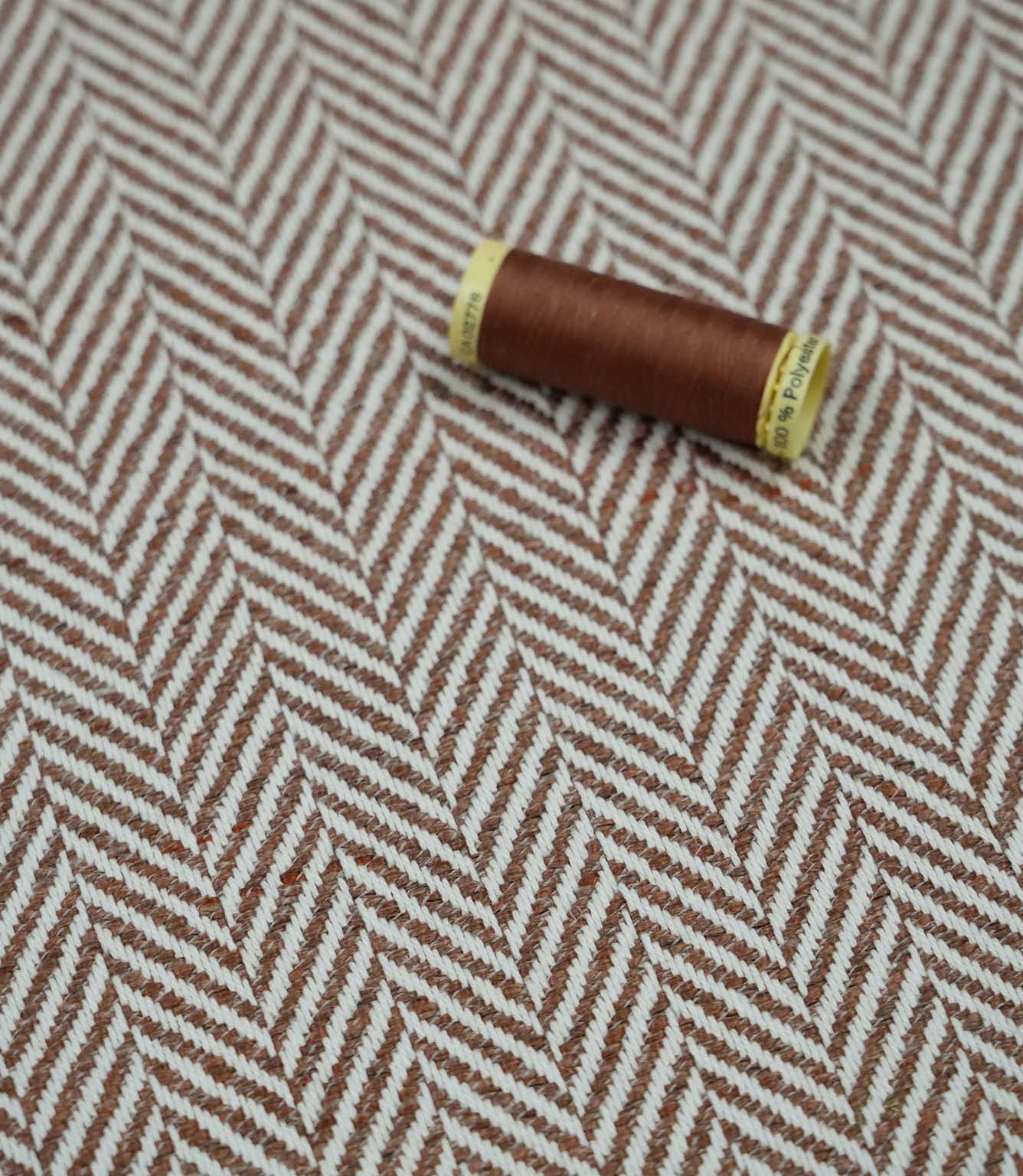 Bampton Terracotta herringbone upholstery fabric with matching terracotta sewing thread, highlighting the woven chevron design and coordinated colour for upholstery and sewing projects.