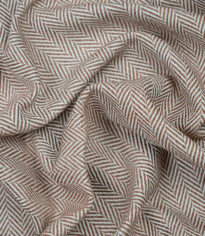 Draped Bampton Terracotta woven fabric showing the natural drape, textured herringbone weave and elegant terracotta and ivory chevron pattern for curtains and home décor.