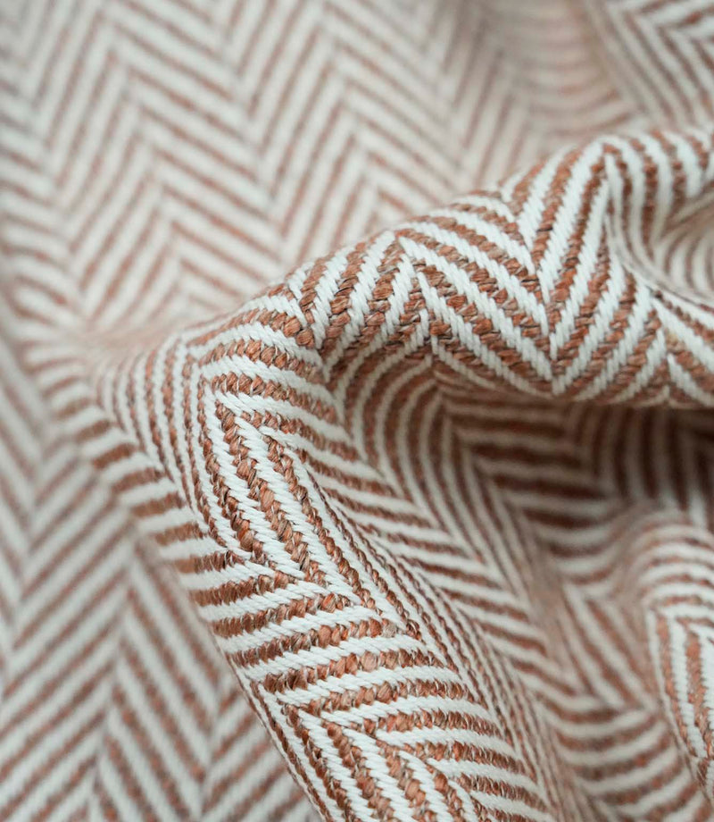 Detailed folded view of Bampton Terracotta herringbone upholstery fabric showing the depth of the woven chevron pattern, durable texture and soft finish for premium home furnishings.