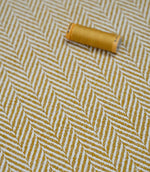 Bampton Turmeric herringbone fabric with a matching turmeric thread spool highlighting the woven texture and coordinated colour.