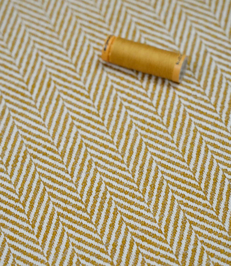 Bampton Turmeric herringbone fabric with a matching turmeric thread spool highlighting the woven texture and coordinated colour.