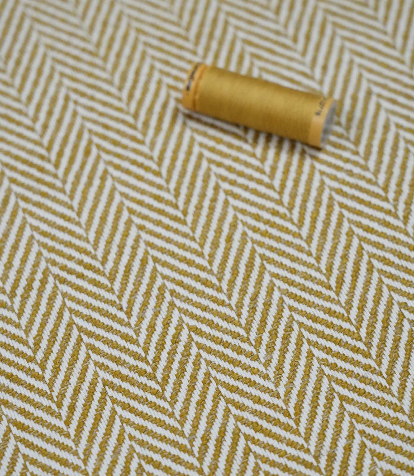 Bampton Turmeric herringbone fabric with a matching turmeric thread spool highlighting the woven texture and coordinated colour.
