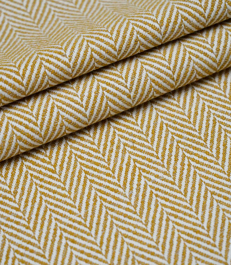 Layered folds of Bampton Turmeric upholstery fabric displaying the textured woven herringbone pattern and fabric depth.