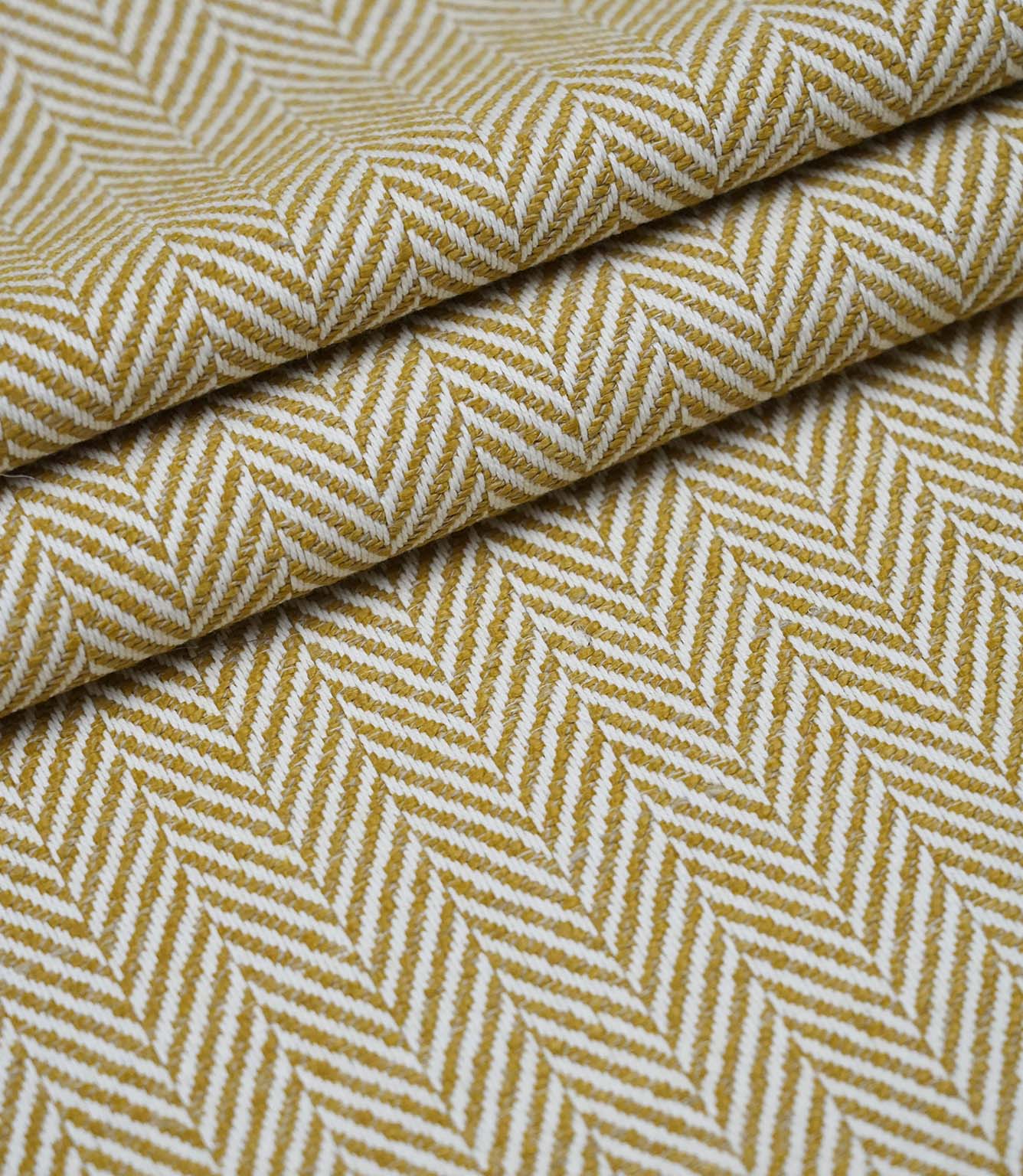 Layered folds of Bampton Turmeric upholstery fabric displaying the textured woven herringbone pattern and fabric depth.