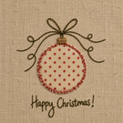 A close-up of a fabric ornament design on a beige woven background, featuring a round ornament with small red stars, a red stitched border, a dark brown bow above it, and the words 'Happy Christmas!' stitched below.