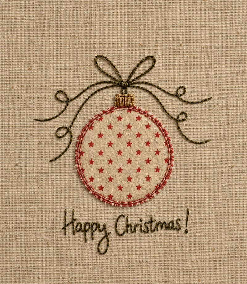 A close-up of a fabric ornament design on a beige woven background, featuring a round ornament with small red stars, a red stitched border, a dark brown bow above it, and the words 'Happy Christmas!' stitched below.