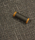 Bellmere Slate upholstery fabric displayed with a coordinating dark grey sewing thread, showcasing the fabric's textured surface and woven construction.