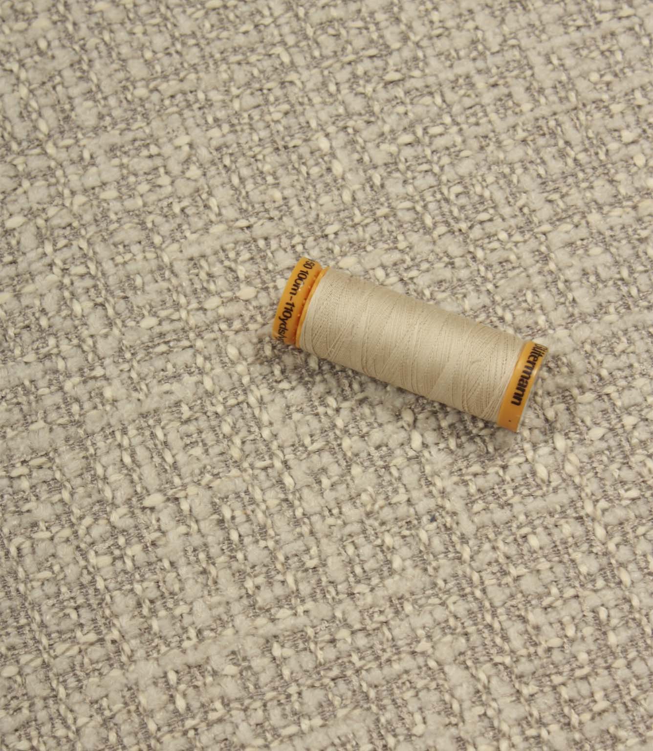 Bellmere Stone upholstery fabric displayed with a coordinating cream sewing thread, showcasing the fabric's textured surface and woven construction.