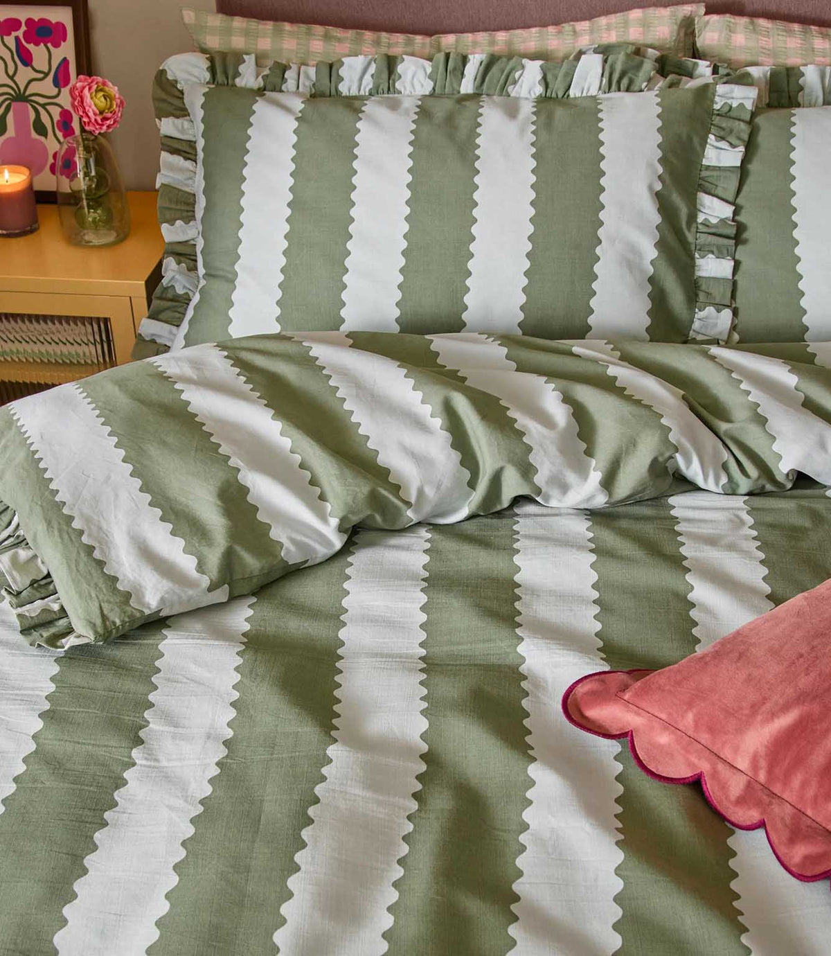 Close-up of the Birdie Stripe Ruffle bedding in sage green and white, showing the scalloped striped duvet cover, gathered ruffle pillowcase edges and soft fabric texture, styled with a pink scalloped cushion.