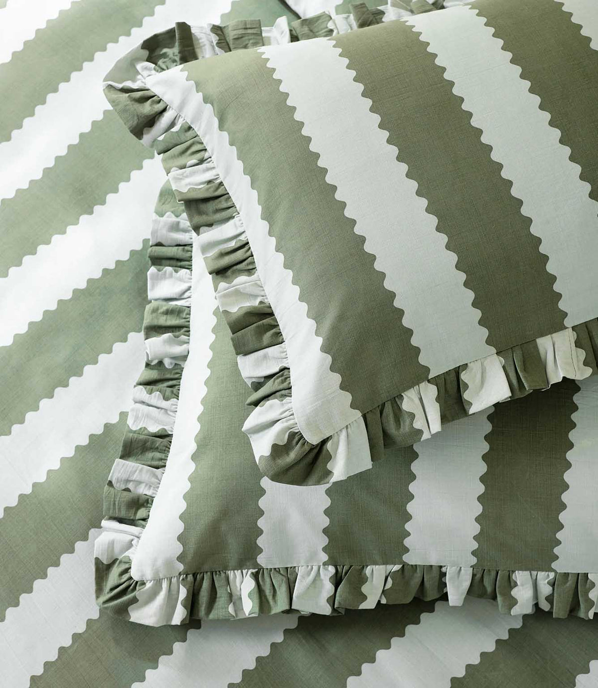 Detailed close-up of the Birdie Stripe Ruffle pillowcase and duvet cover in sage green and white, showing the wide scalloped stripe pattern, subtle woven texture and gathered ruffle trim.