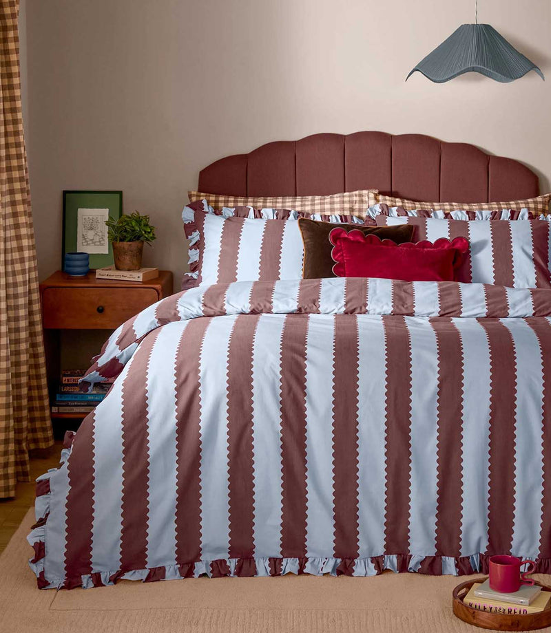 Birdie Stripe Ruffle duvet cover set in chocolate brown and pale blue, featuring wide scalloped vertical stripes and gathered ruffle edging, styled on a bed with coordinating pillows.